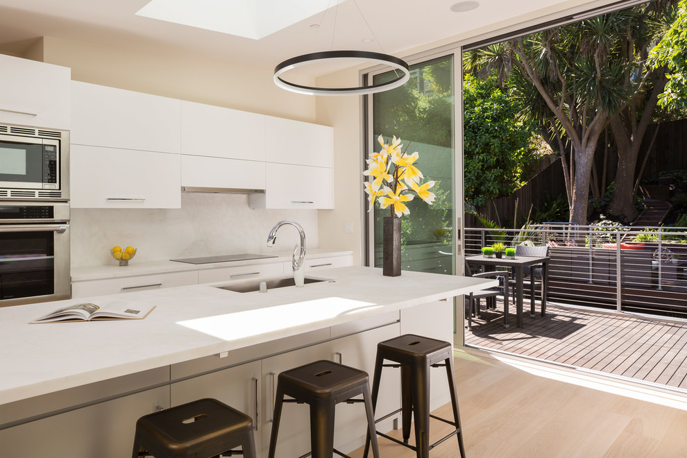 Photo of a contemporary kitchen in Los Angeles with an undermount sink, flat-panel cabinets, white cabinets, white splashback, stainless steel appliances, light hardwood floors and with island.
