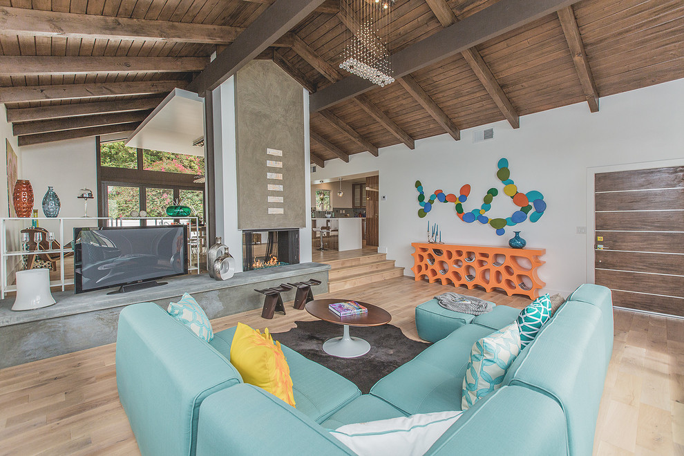 This is an example of a large midcentury open concept living room in Los Angeles with white walls, light hardwood floors, a two-sided fireplace, a concrete fireplace surround and a freestanding tv.