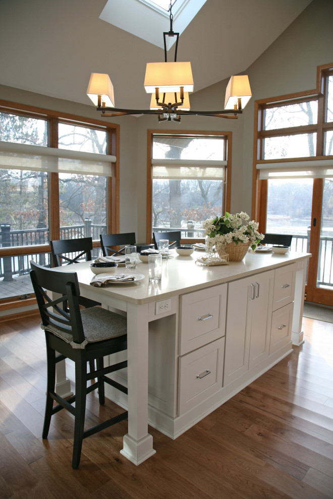 Bild på ett stort maritimt vit vitt kök och matrum, med en undermonterad diskho, skåp i shakerstil, vita skåp, bänkskiva i kvarts, vitt stänkskydd, stänkskydd i porslinskakel, rostfria vitvaror, ljust trägolv, flera köksöar och brunt golv