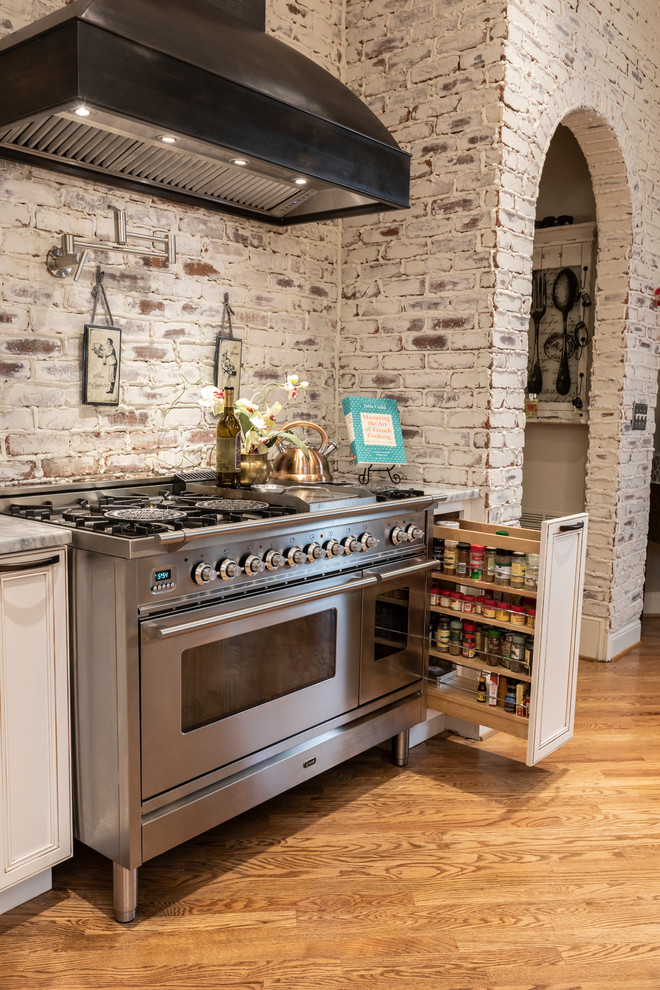Photo of a large traditional open plan kitchen in Atlanta with a farmhouse sink, flat-panel cabinets, white cabinets, limestone benchtops, red splashback, brick splashback, stainless steel appliances, light hardwood floors, multiple islands, brown floor and grey benchtop.