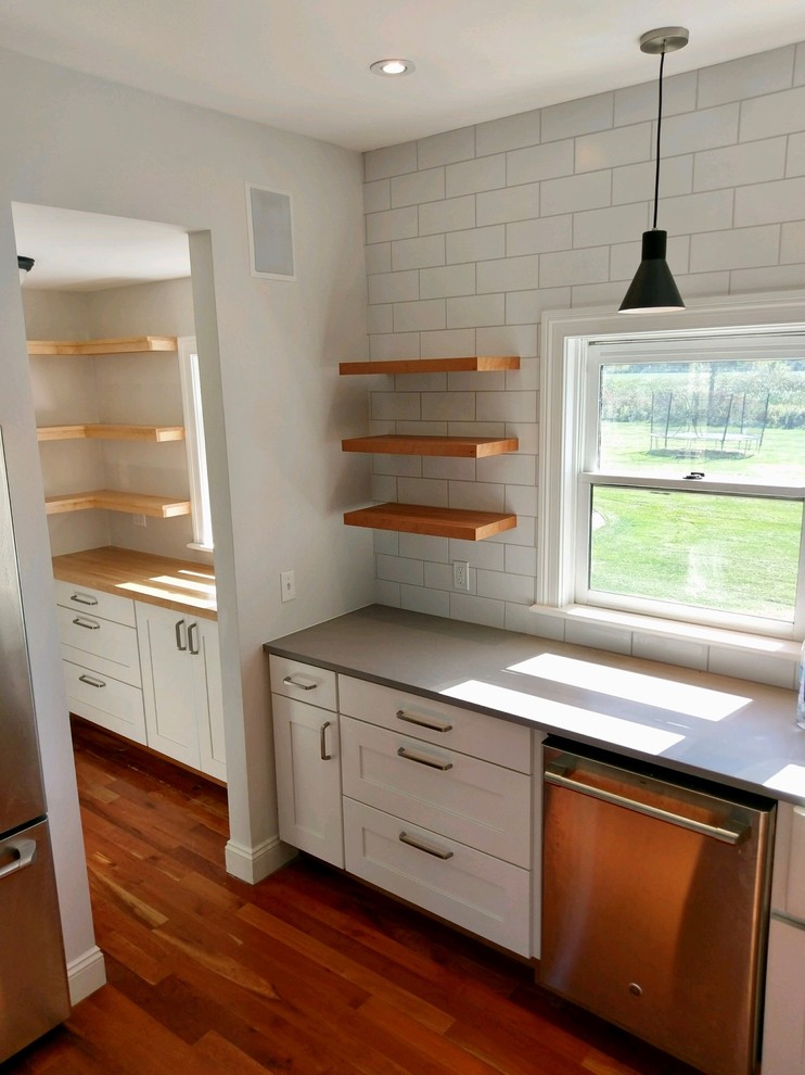 Design ideas for a mid-sized country galley eat-in kitchen in Portland with a farmhouse sink, shaker cabinets, white cabinets, quartz benchtops, white splashback, subway tile splashback, stainless steel appliances, medium hardwood floors, with island, orange floor and grey benchtop.