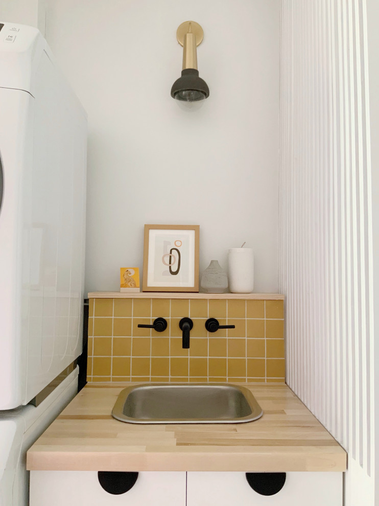 Inspiration for an eclectic laundry room in Los Angeles with a drop-in sink, white cabinets and yellow splashback.