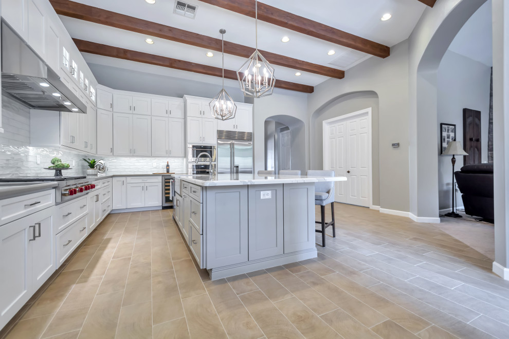 Inspiration for a large transitional l-shaped porcelain tile and brown floor eat-in kitchen remodel in Phoenix with a farmhouse sink, shaker cabinets, white cabinets, quartz countertops, white backsplash, subway tile backsplash, stainless steel appliances, an island and gray countertops