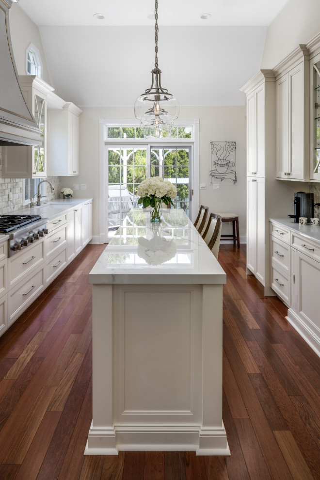 Inspiration for a large traditional galley separate kitchen in Detroit with an undermount sink, raised-panel cabinets, white cabinets, quartz benchtops, white splashback, marble splashback, panelled appliances, medium hardwood floors, with island, red floor and white benchtop.