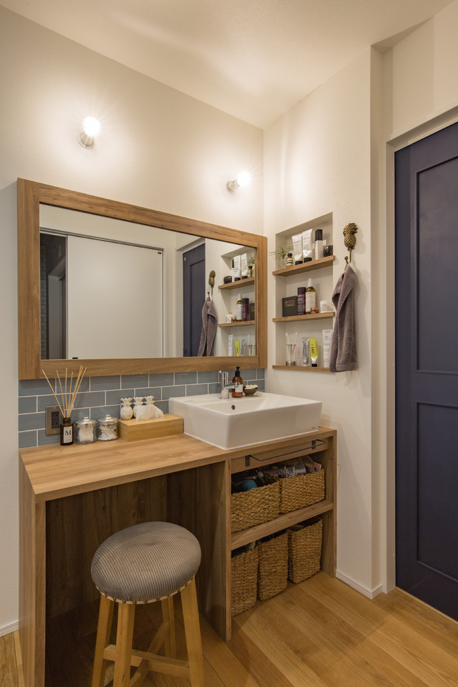 Photo of a beach style powder room in Other with open cabinets, medium wood cabinets, white walls, medium hardwood floors, a vessel sink, wood benchtops, brown floor and brown benchtops.