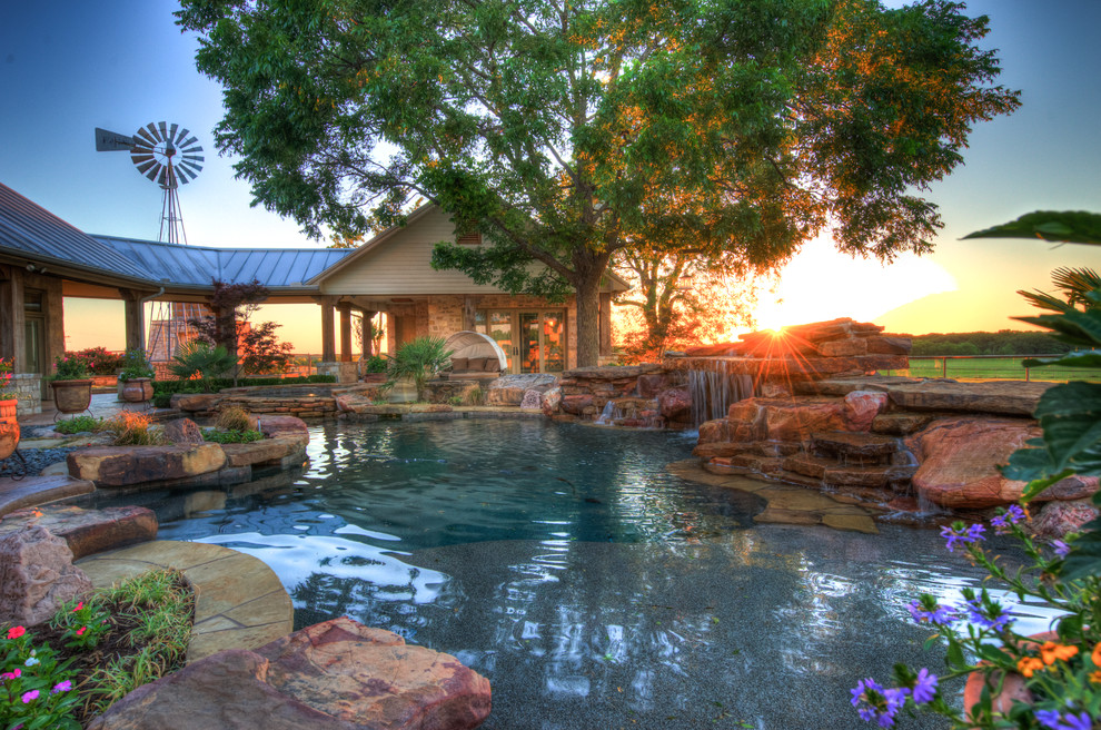Design ideas for an expansive tropical backyard custom-shaped natural pool in Austin with a hot tub and natural stone pavers.