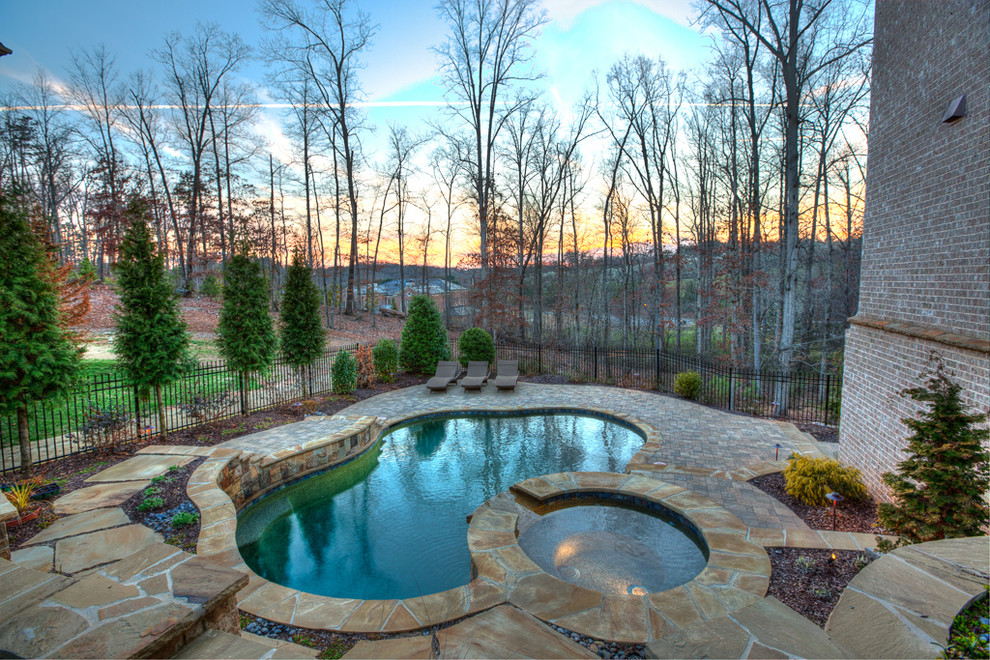 This is an example of a mid-sized traditional backyard custom-shaped pool in Atlanta with a hot tub and natural stone pavers.