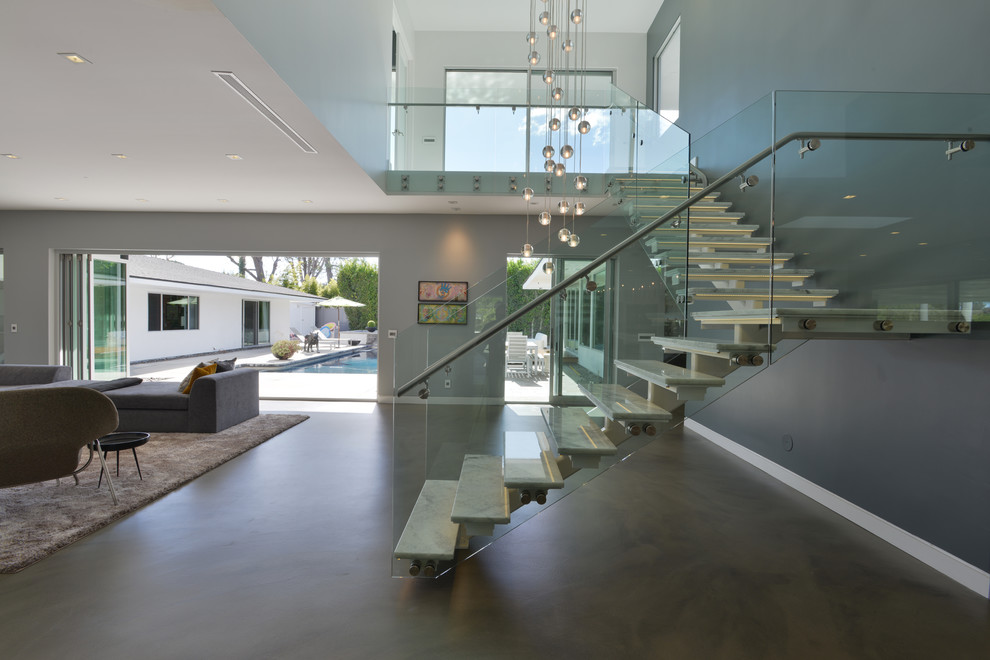 This is an example of a mid-sized modern marble l-shaped staircase in Los Angeles with open risers and glass railing.