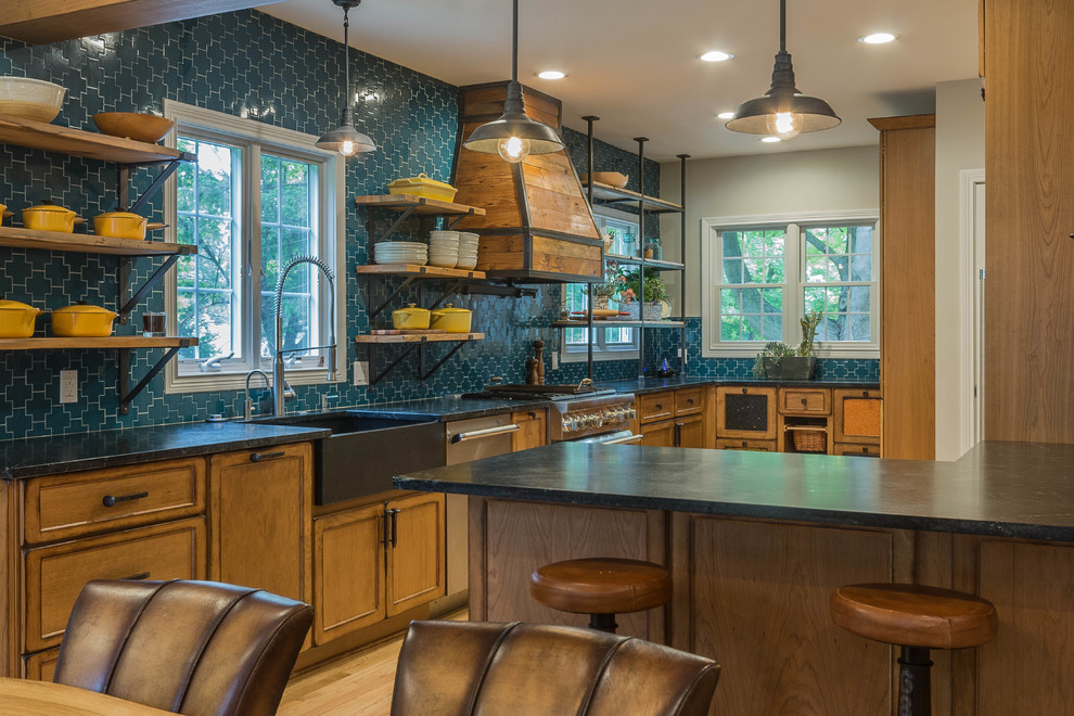 Inspiration for a large arts and crafts l-shaped eat-in kitchen in Detroit with a farmhouse sink, flat-panel cabinets, medium wood cabinets, soapstone benchtops, blue splashback, porcelain splashback, stainless steel appliances, light hardwood floors, a peninsula, brown floor and brown benchtop.