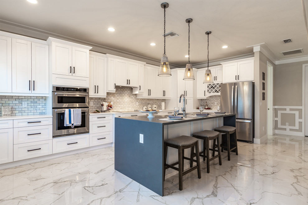 Photo of a transitional l-shaped kitchen in Tampa with a farmhouse sink, shaker cabinets, white cabinets, multi-coloured splashback, subway tile splashback, stainless steel appliances, marble floors, with island, multi-coloured floor and white benchtop.