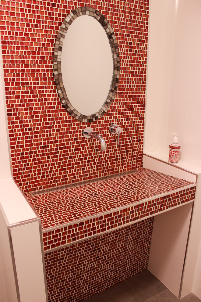 Design ideas for a mid-sized contemporary bathroom in Vancouver with red tile, glass sheet wall, red walls, porcelain floors, a trough sink, tile benchtops and grey floor.
