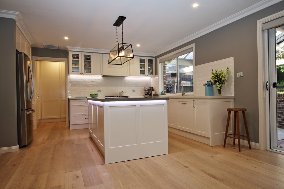 Photo of a large eclectic l-shaped kitchen pantry in Sydney with an undermount sink, shaker cabinets, white cabinets, quartz benchtops, white splashback, subway tile splashback, stainless steel appliances, light hardwood floors, with island and brown floor.
