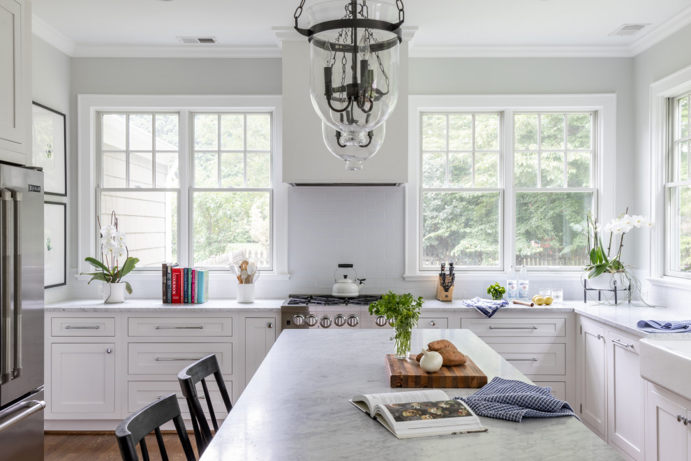 Foto på ett stort vintage vit u-kök, med en undermonterad diskho, luckor med infälld panel, vita skåp, marmorbänkskiva, vitt stänkskydd, stänkskydd i keramik, rostfria vitvaror, mellanmörkt trägolv, en köksö och brunt golv