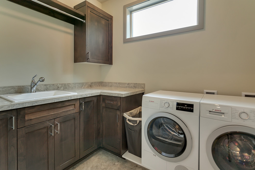 Inspiration for a mid-sized transitional l-shaped dedicated laundry room in Portland with a drop-in sink, shaker cabinets, medium wood cabinets, tile benchtops, grey walls, ceramic floors and a side-by-side washer and dryer.