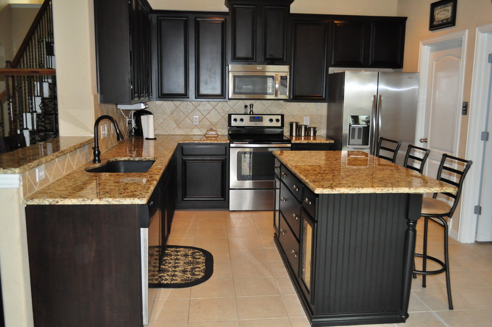 This is an example of a mid-sized arts and crafts l-shaped eat-in kitchen in Dallas with an undermount sink, recessed-panel cabinets, black cabinets, granite benchtops, beige splashback, stone tile splashback, stainless steel appliances, ceramic floors, with island, beige floor and beige benchtop.