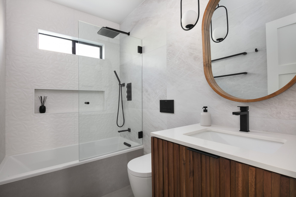 This is an example of a small modern master bathroom in Los Angeles with dark wood cabinets, a drop-in tub, a shower/bathtub combo, a wall-mount toilet, gray tile, porcelain tile, porcelain floors, an undermount sink, engineered quartz benchtops, grey floor, an open shower, white benchtops, a niche, a single vanity, a freestanding vanity and flat-panel cabinets.