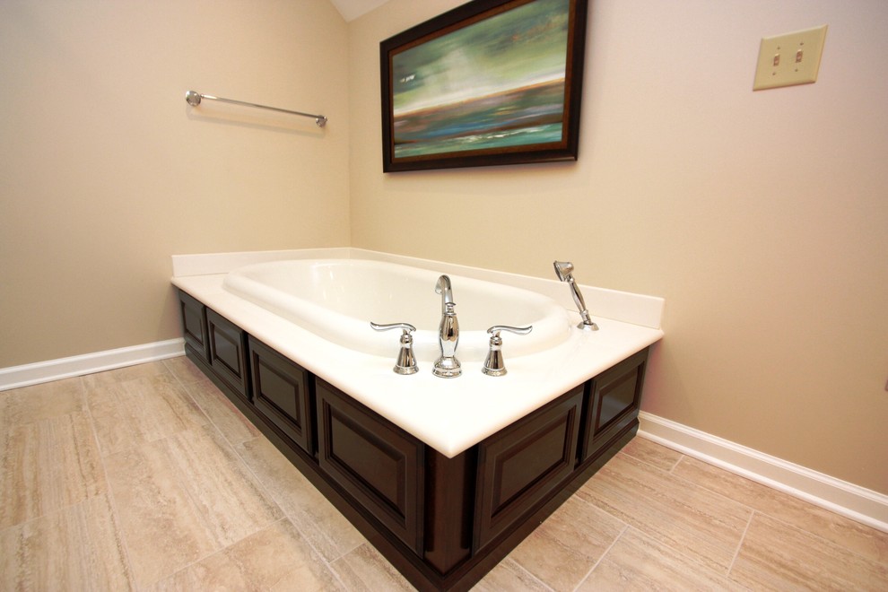 Large transitional master bathroom in Raleigh with an integrated sink, raised-panel cabinets, dark wood cabinets, marble benchtops, a drop-in tub, a corner shower, a one-piece toilet, beige tile, porcelain tile, beige walls and porcelain floors.
