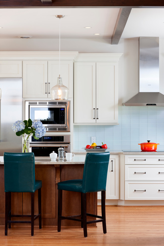 Example of a classic medium tone wood floor kitchen design with shaker cabinets, white cabinets, blue backsplash, stainless steel appliances, white walls and an island