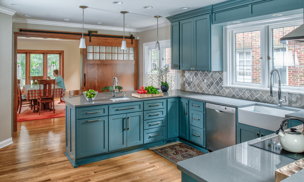 Mid-sized arts and crafts u-shaped separate kitchen in Indianapolis with a farmhouse sink, shaker cabinets, blue cabinets, quartz benchtops, beige splashback, ceramic splashback, stainless steel appliances, medium hardwood floors, a peninsula and brown floor.