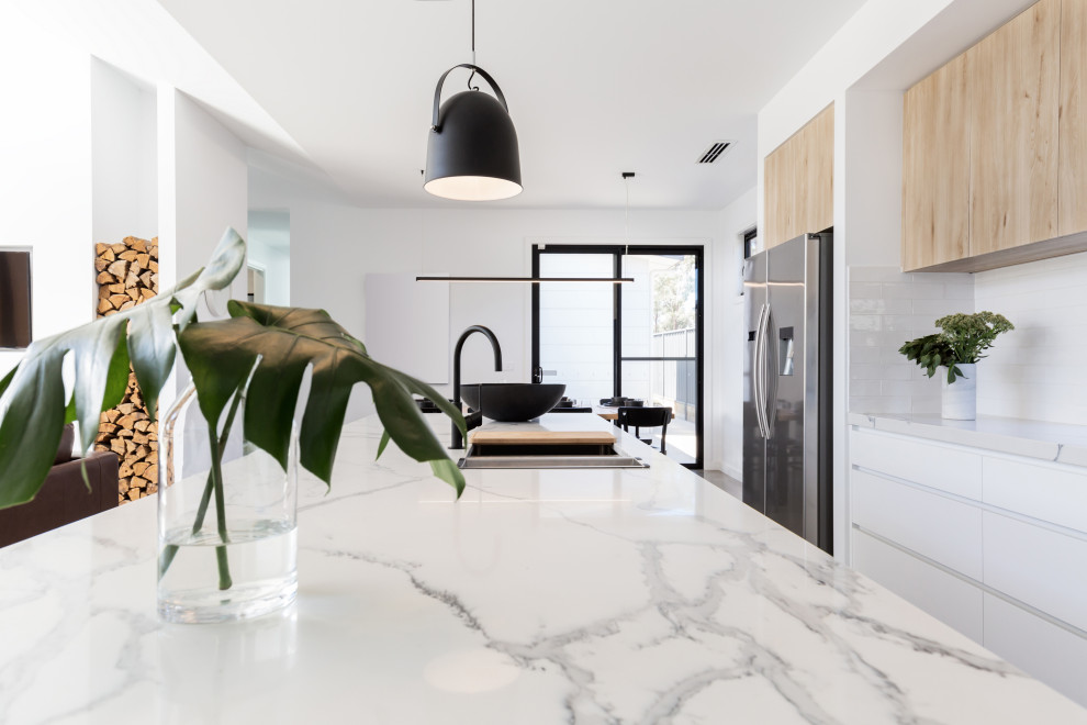 This is an example of a large scandinavian l-shaped open plan kitchen in Malaga with a farmhouse sink, flat-panel cabinets, white cabinets, quartz benchtops, white splashback, ceramic splashback, stainless steel appliances, concrete floors, with island, brown floor and white benchtop.