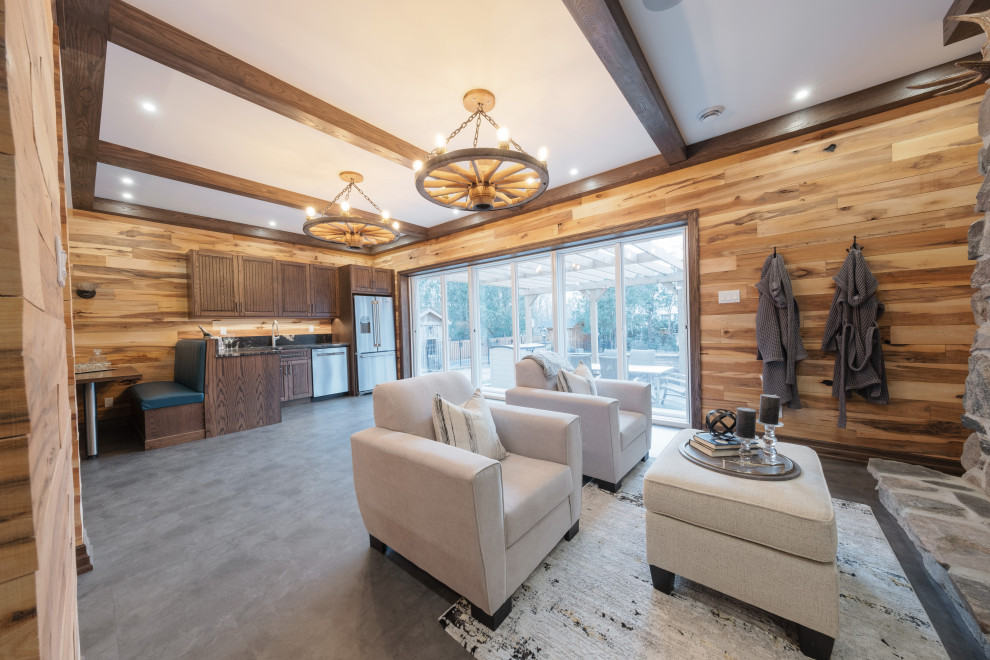 Large mountain style walk-out vinyl floor, gray floor, exposed beam and wood wall basement photo with a bar, multicolored walls, a standard fireplace and a stone fireplace