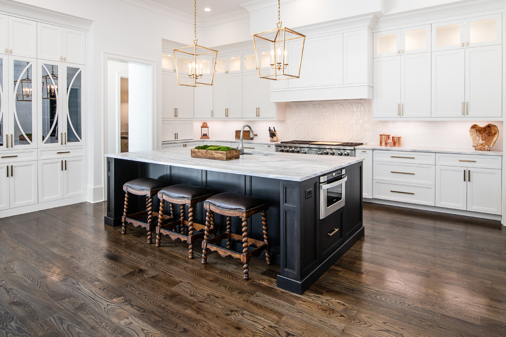 Photo of a large transitional kitchen in Charlotte with white cabinets, quartzite benchtops, white splashback, ceramic splashback, dark hardwood floors, with island, white benchtop, an undermount sink, recessed-panel cabinets, stainless steel appliances and brown floor.