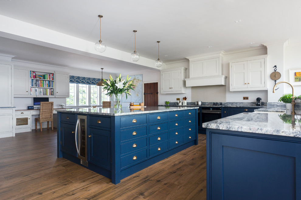 This is an example of a transitional open plan kitchen in Kent with a farmhouse sink, beaded inset cabinets, blue cabinets, granite benchtops, black splashback, glass sheet splashback and with island.