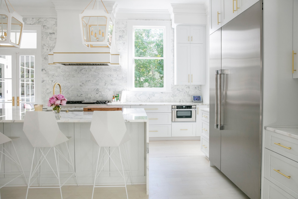 Photo of a large traditional single-wall kitchen/diner in New Orleans with a submerged sink, shaker cabinets, white cabinets, white splashback, stainless steel appliances, light hardwood flooring and an island.