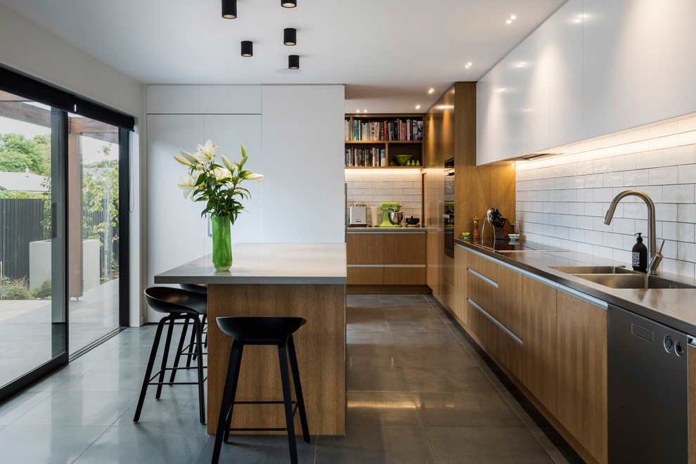Design ideas for a contemporary galley kitchen in Christchurch with an integrated sink, flat-panel cabinets, medium wood cabinets, white splashback, subway tile splashback, stainless steel appliances, with island, grey floor and grey benchtop.