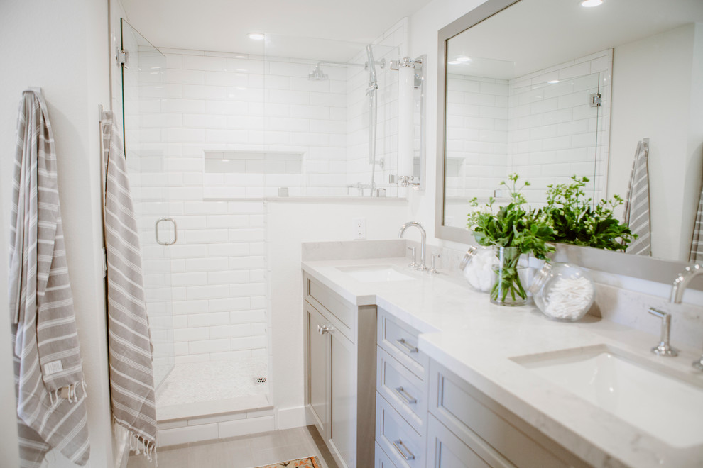 Photo of a mid-sized beach style master bathroom in San Diego with shaker cabinets, grey cabinets, an alcove shower, a one-piece toilet, white tile, porcelain tile, white walls, ceramic floors, an undermount sink, engineered quartz benchtops, grey floor and a hinged shower door.