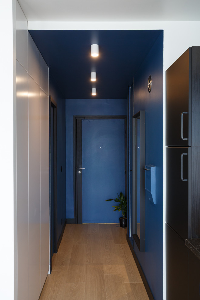 Inspiration pour une entrée nordique de taille moyenne avec un couloir, un mur bleu, parquet clair, une porte simple, une porte bleue et un sol marron.