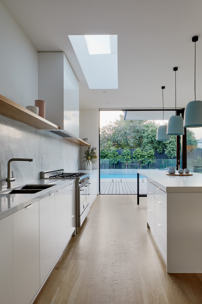 Idéer för ett modernt linjärt kök med öppen planlösning, med en undermonterad diskho, marmorbänkskiva, stänkskydd i marmor, rostfria vitvaror, ljust trägolv och en köksö