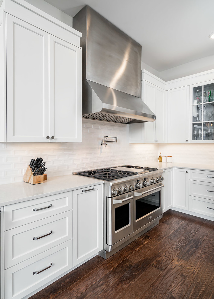 Example of a mid-sized transitional u-shaped dark wood floor and brown floor open concept kitchen design with an undermount sink, shaker cabinets, white cabinets, quartz countertops, white backsplash, ceramic backsplash, stainless steel appliances and an island
