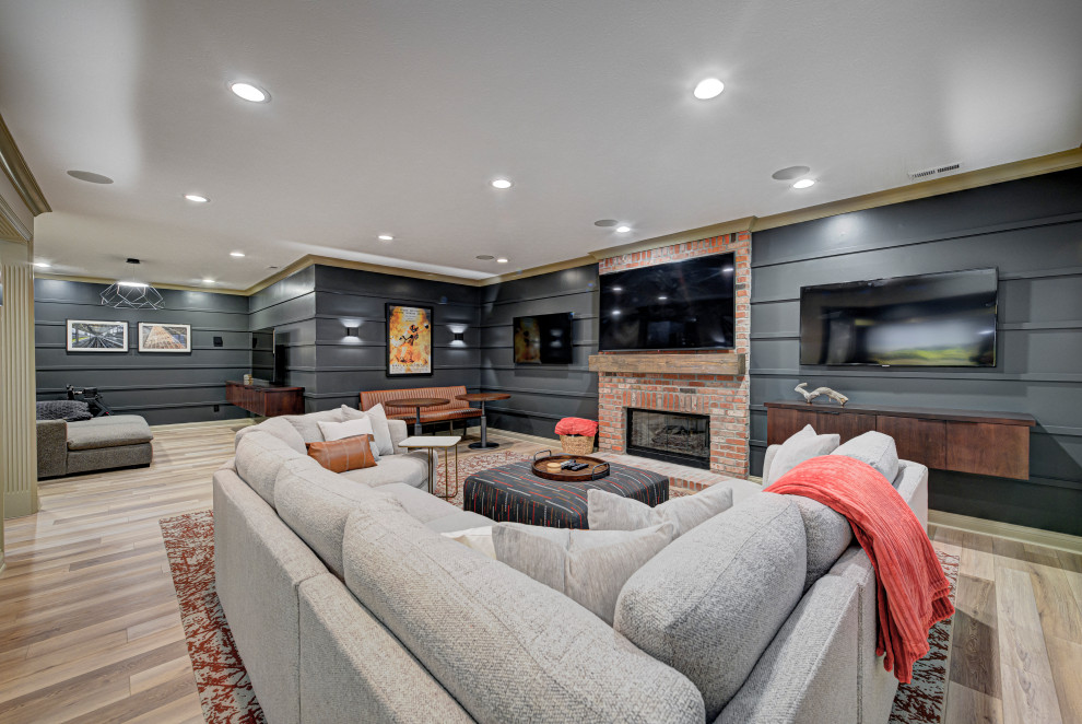 Design ideas for a mid-sized contemporary fully buried basement in Indianapolis with a standard fireplace, grey walls, light hardwood floors, a brick fireplace surround, brown floor and panelled walls.