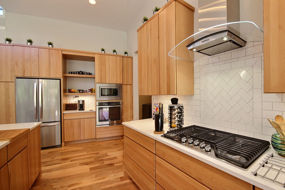 Huge minimalist l-shaped medium tone wood floor and brown floor open concept kitchen photo in Portland with an undermount sink, flat-panel cabinets, medium tone wood cabinets, quartz countertops, white backsplash, ceramic backsplash, stainless steel appliances, an island and white countertops