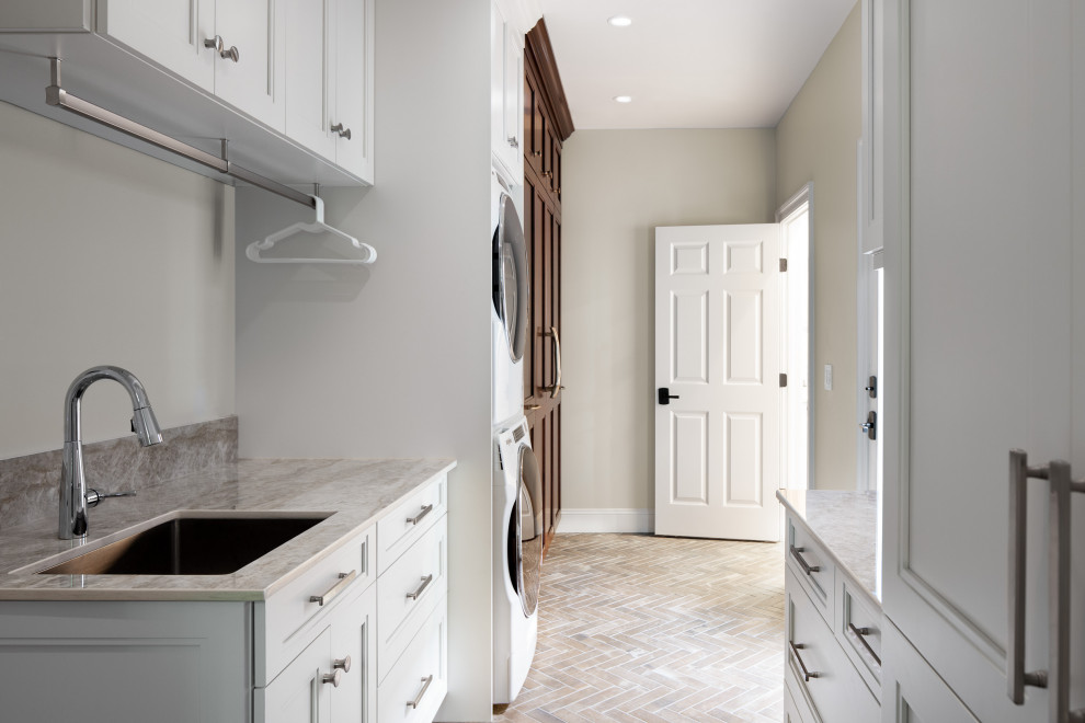 This is an example of a mid-sized transitional galley utility room in Raleigh with a single-bowl sink, recessed-panel cabinets, white cabinets, quartz benchtops, white walls, ceramic floors, a stacked washer and dryer, beige floor and beige benchtop.