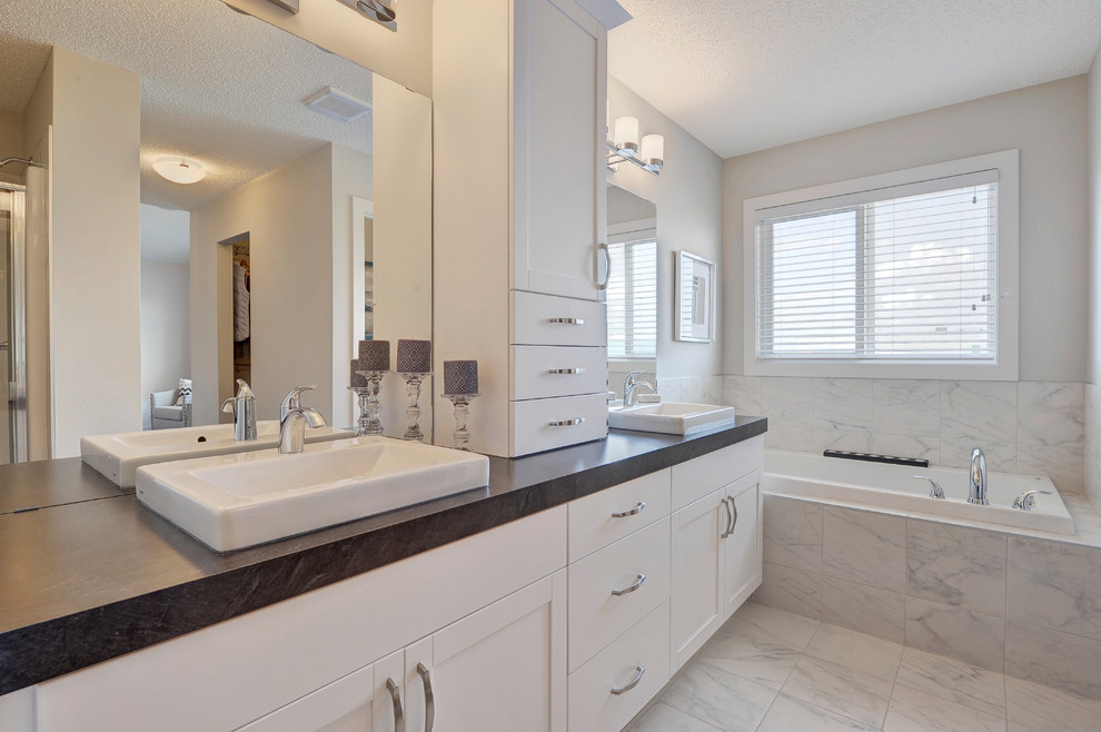Example of a mid-sized transitional master gray tile and ceramic tile ceramic tile and white floor alcove bathtub design in Edmonton with shaker cabinets, white cabinets, a two-piece toilet, gray walls, a vessel sink, laminate countertops and a hinged shower door