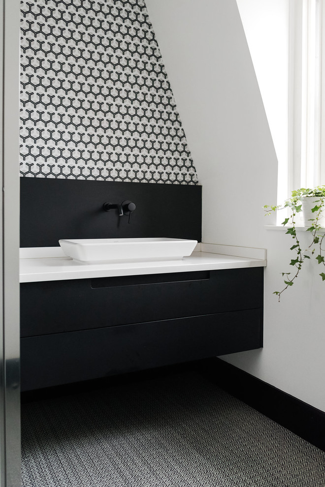 This is an example of a small modern kids bathroom in London with flat-panel cabinets, black cabinets, a corner shower, a one-piece toilet, multi-coloured tile, ceramic tile, white walls, vinyl floors, a console sink, solid surface benchtops, black floor and a hinged shower door.