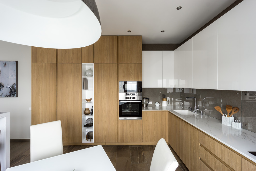Inspiration for a mid-sized contemporary l-shaped eat-in kitchen in Moscow with an undermount sink, flat-panel cabinets, medium wood cabinets, solid surface benchtops, grey splashback, glass sheet splashback, stainless steel appliances, porcelain floors, no island, brown floor and white benchtop.