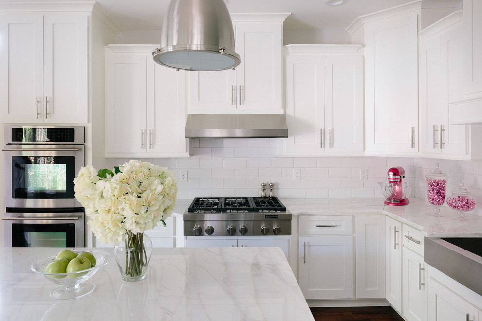 Example of a large transitional u-shaped dark wood floor eat-in kitchen design in Atlanta with a farmhouse sink, shaker cabinets, white cabinets, marble countertops, white backsplash, ceramic backsplash, stainless steel appliances and an island