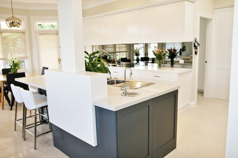 Photo of a large transitional l-shaped eat-in kitchen in Sydney with a drop-in sink, shaker cabinets, white cabinets, quartz benchtops, grey splashback, glass sheet splashback, stainless steel appliances, ceramic floors and with island.