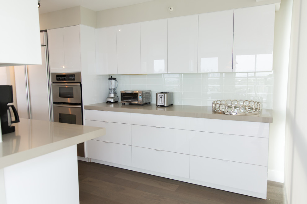 This is an example of a large modern l-shaped open plan kitchen in San Diego with an undermount sink, flat-panel cabinets, white cabinets, quartz benchtops, white splashback, stainless steel appliances, light hardwood floors, no island, glass tile splashback and brown floor.