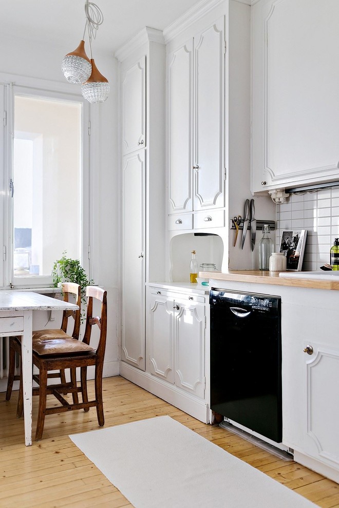 Design ideas for a mid-sized traditional single-wall eat-in kitchen in Stockholm with recessed-panel cabinets, white cabinets, wood benchtops, white splashback, black appliances, medium hardwood floors and no island.