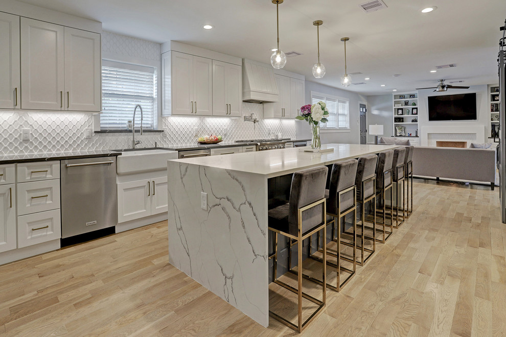 Example of a mid-sized transitional galley light wood floor and yellow floor eat-in kitchen design in Houston with a farmhouse sink, recessed-panel cabinets, white cabinets, quartz countertops, white backsplash, ceramic backsplash, stainless steel appliances, an island and white countertops
