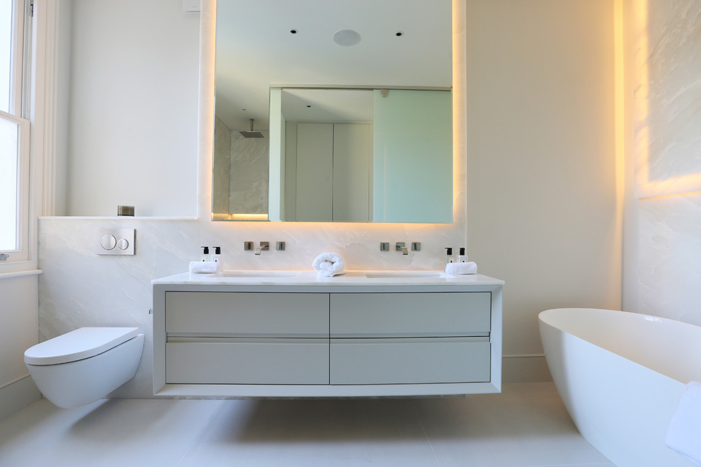 Inspiration for a mid-sized modern bathroom in London with flat-panel cabinets, beige cabinets, a freestanding tub, a wall-mount toilet, white tile, a wall-mount sink, white floor, white benchtops and white walls.
