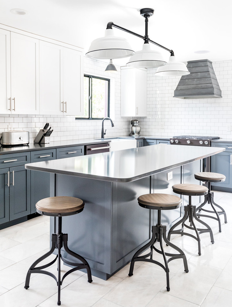 Photo of a large country l-shaped separate kitchen in Wilmington with a farmhouse sink, shaker cabinets, blue cabinets, quartz benchtops, white splashback, subway tile splashback, black appliances, marble floors, with island, grey floor and black benchtop.