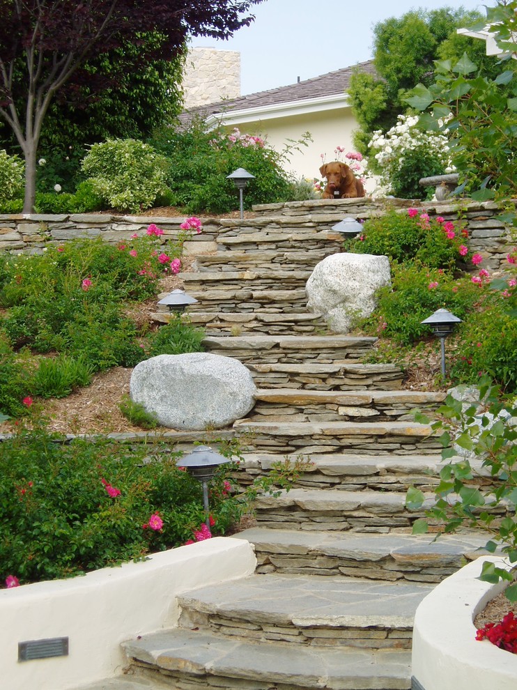 Photo of a traditional sloped full sun garden in San Diego with a retaining wall and natural stone pavers.