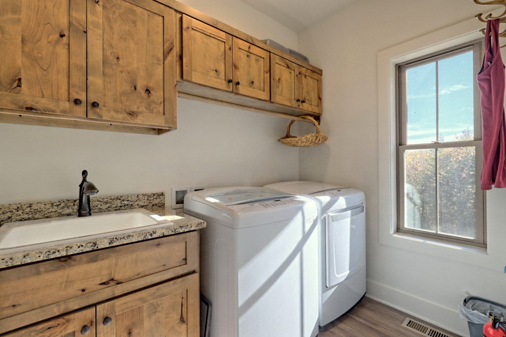 This is an example of a mid-sized arts and crafts single-wall dedicated laundry room in Atlanta with a drop-in sink, shaker cabinets, light wood cabinets, granite benchtops, white walls, vinyl floors, a side-by-side washer and dryer, brown floor and multi-coloured benchtop.