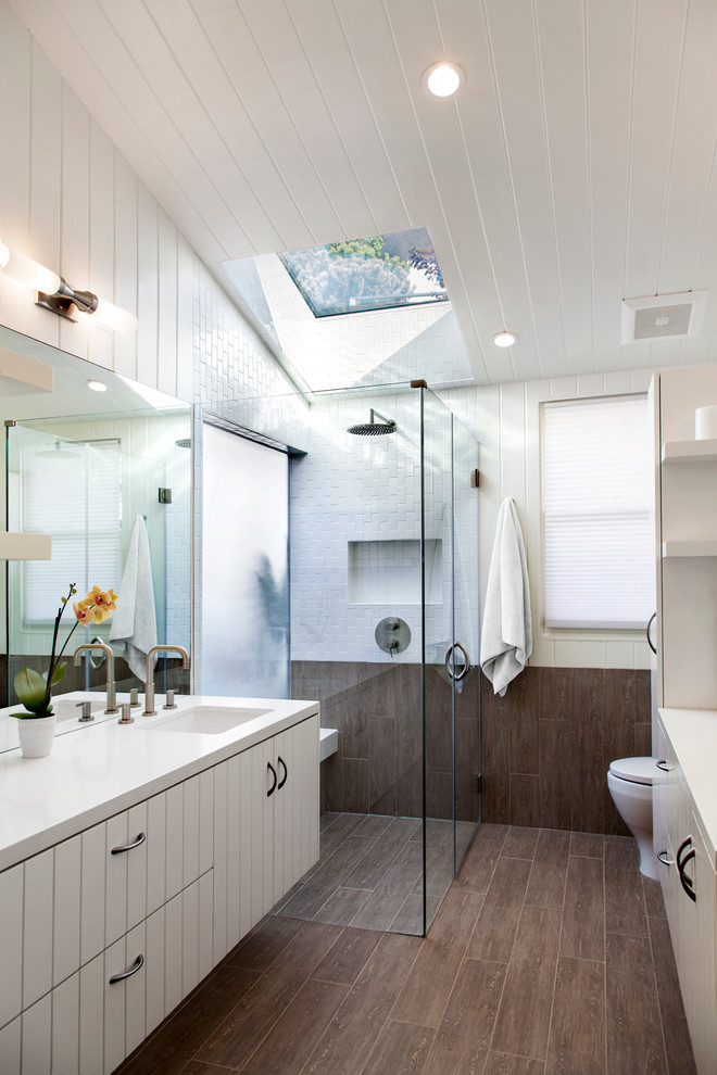 This is an example of a transitional bathroom in Los Angeles with an undermount sink, flat-panel cabinets, white cabinets, a corner shower, gray tile and white walls.