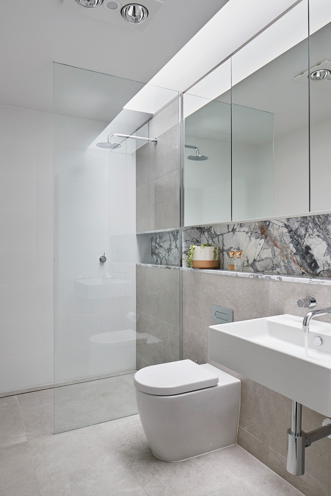 Small modern master bathroom in Melbourne with glass-front cabinets, an open shower, a wall-mount toilet, white tile, ceramic tile, beige walls, ceramic floors, a wall-mount sink, marble benchtops, beige floor, an open shower and white benchtops.